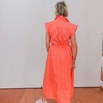 Person wearing an orange striped dress standing against a white wall.