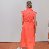 Person wearing an orange striped dress standing against a white wall.