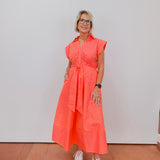 Woman wearing a bright orange dress with white stripes, standing against a plain background.