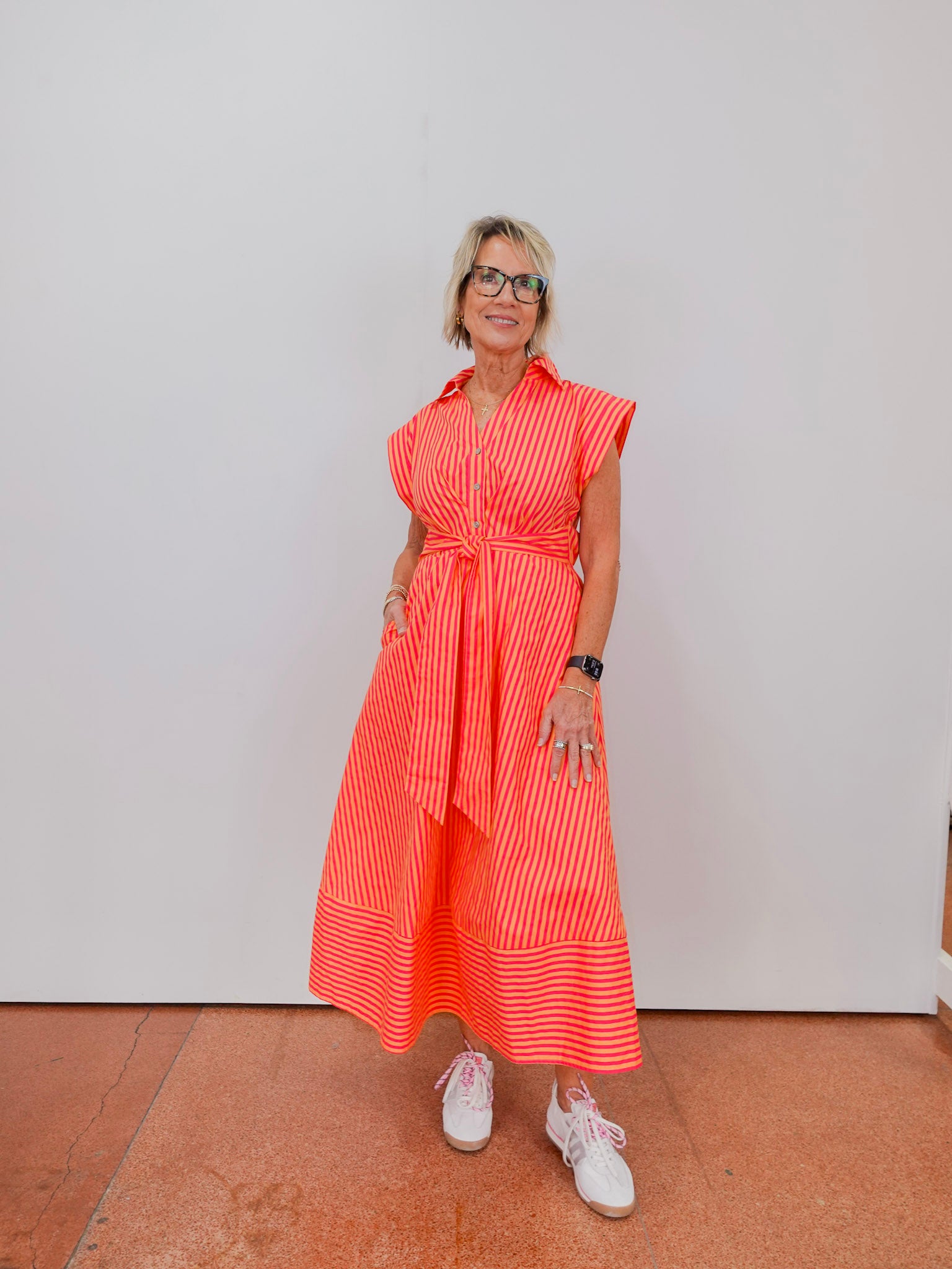 Woman wearing a bright orange dress with white stripes, standing against a plain background.