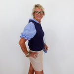 Woman wearing a blue and white striped shirt with a navy vest and beige shorts against a white background