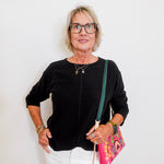 Woman wearing a black top and white pants, holding a colorful bag against a white background