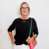 Woman wearing a black top and white pants, holding a colorful bag against a white background
