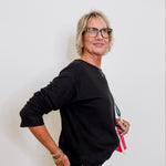 Woman wearing a black sweater and white pants against a plain background