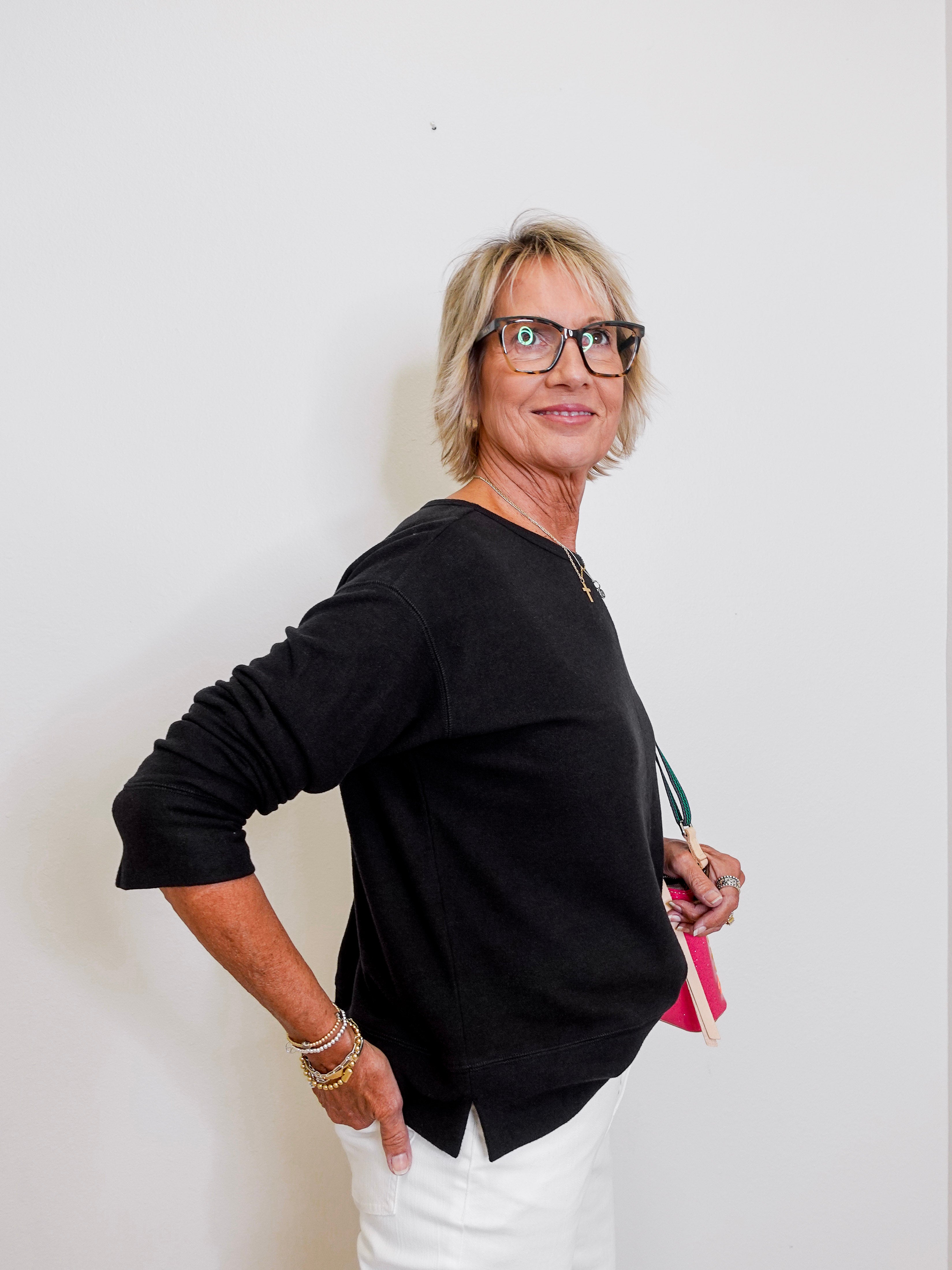 Woman wearing a black sweater and white pants against a plain background