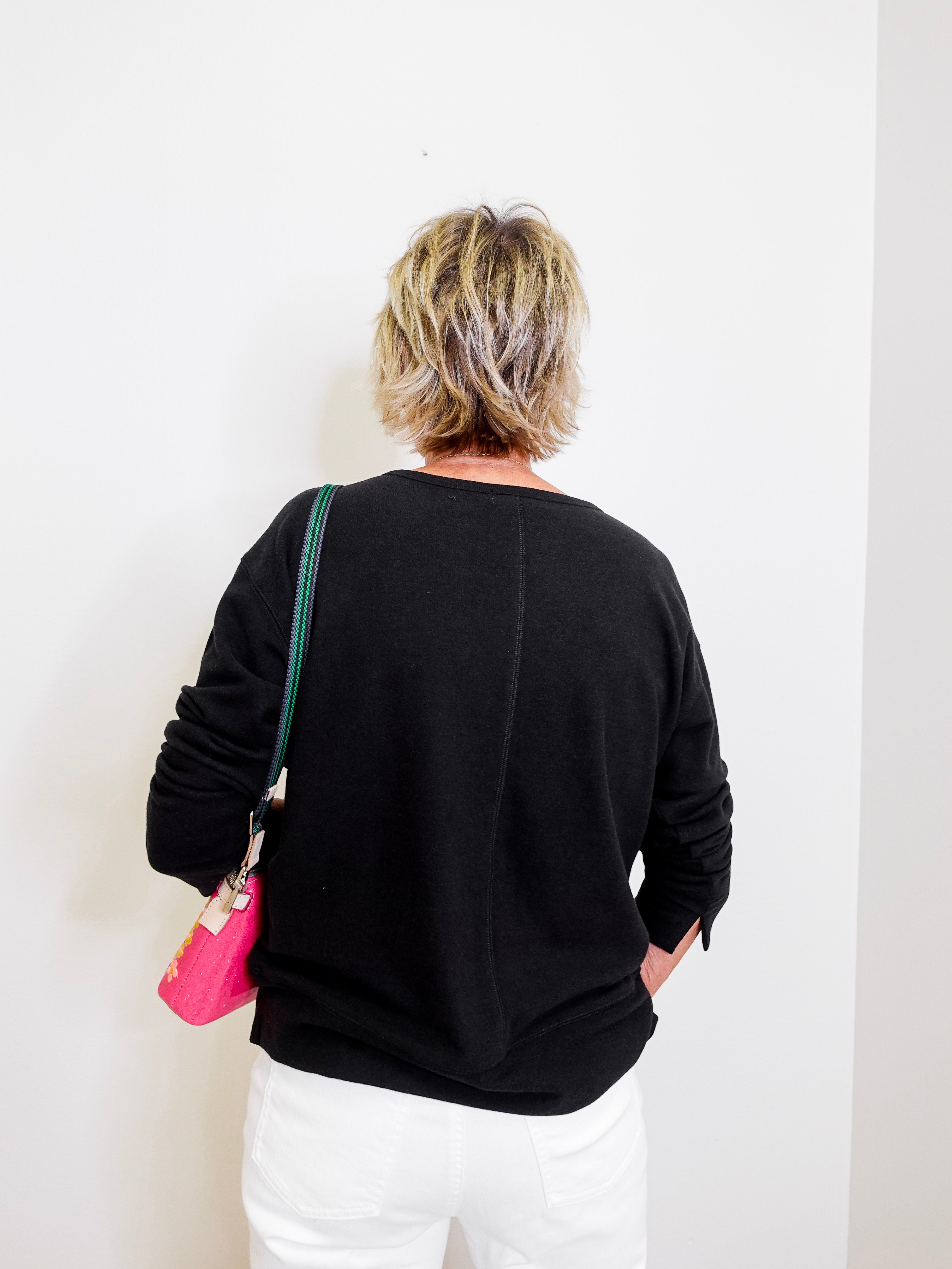 Person wearing a black sweater with a white wall background