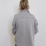 Person wearing a gray jacket against a white wall
