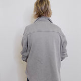 Person wearing a gray jacket against a white wall