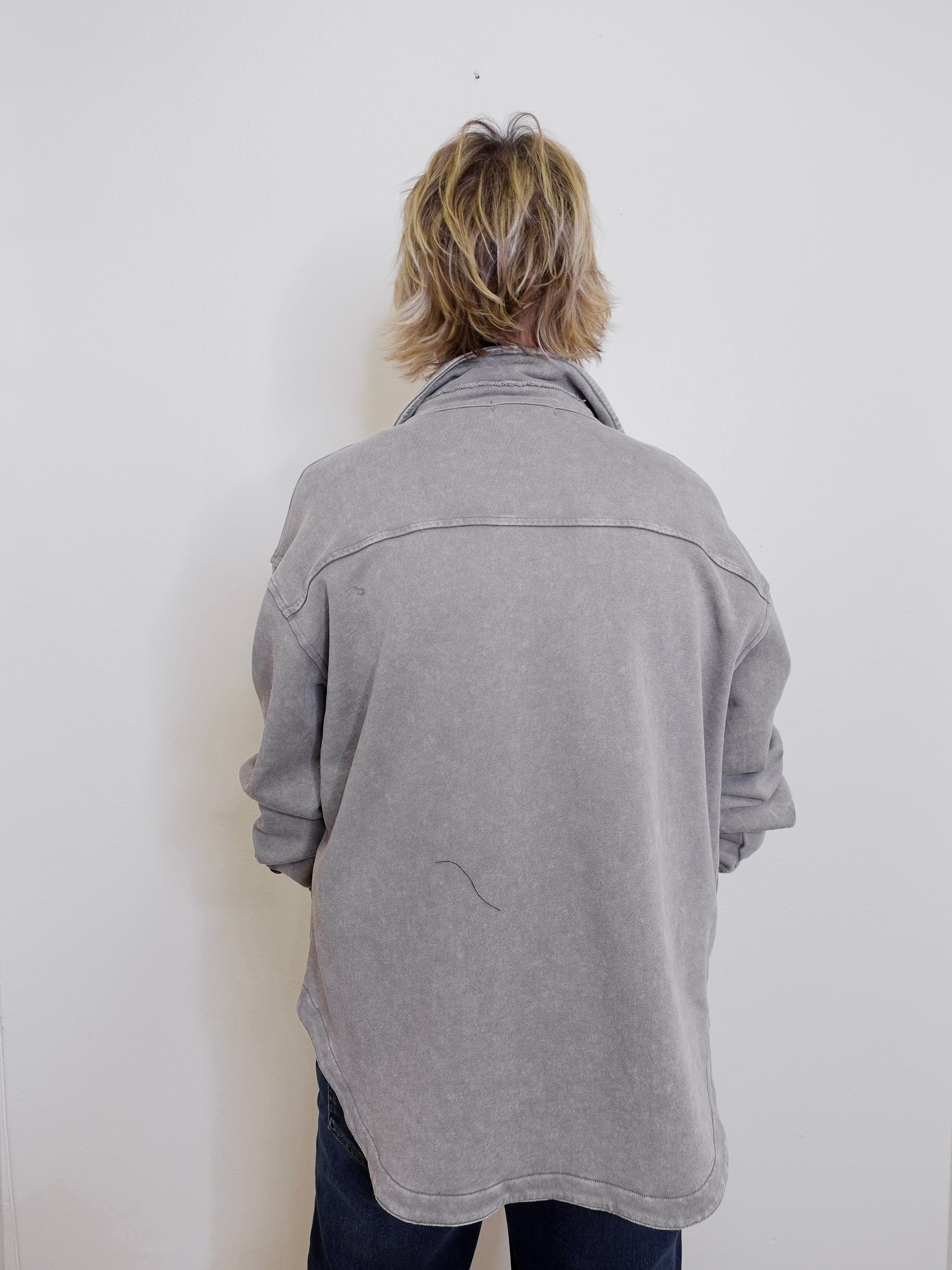 Person wearing a gray jacket against a white wall