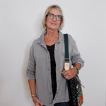 Woman wearing a gray shirt and glasses, holding a black bag with floral patterns against a white background