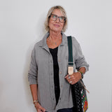 Woman wearing a gray shirt and glasses, holding a black bag with floral patterns against a white background