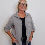 Woman wearing a gray jacket over a black shirt with blue jeans against a white background