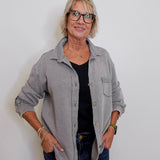 Woman wearing a gray jacket over a black shirt with blue jeans against a white background