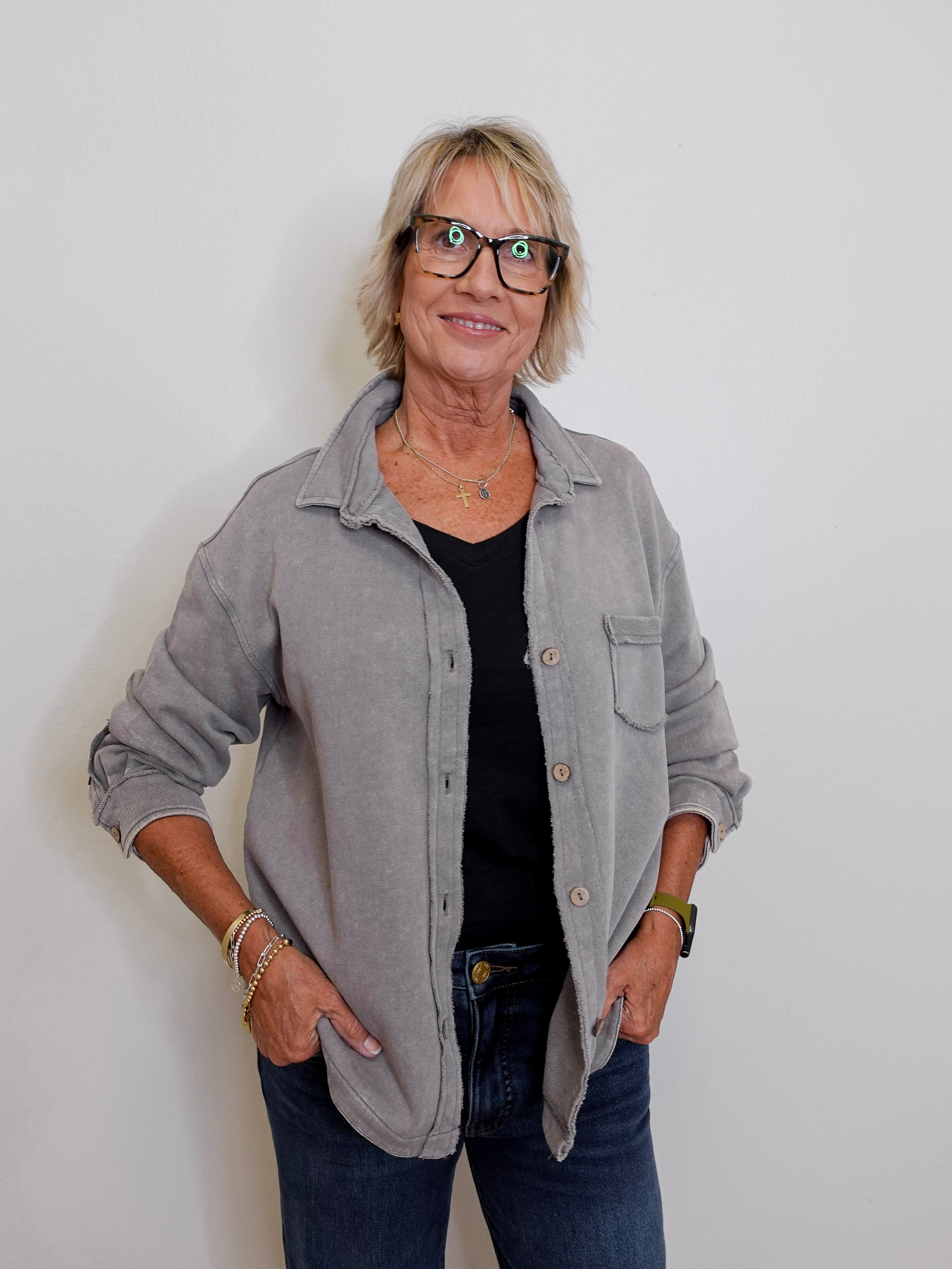Woman wearing a gray jacket over a black shirt with blue jeans against a white background