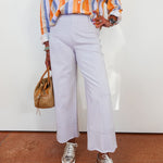 Person wearing a colorful striped shirt, light purple pants, and silver sneakers on a white background.