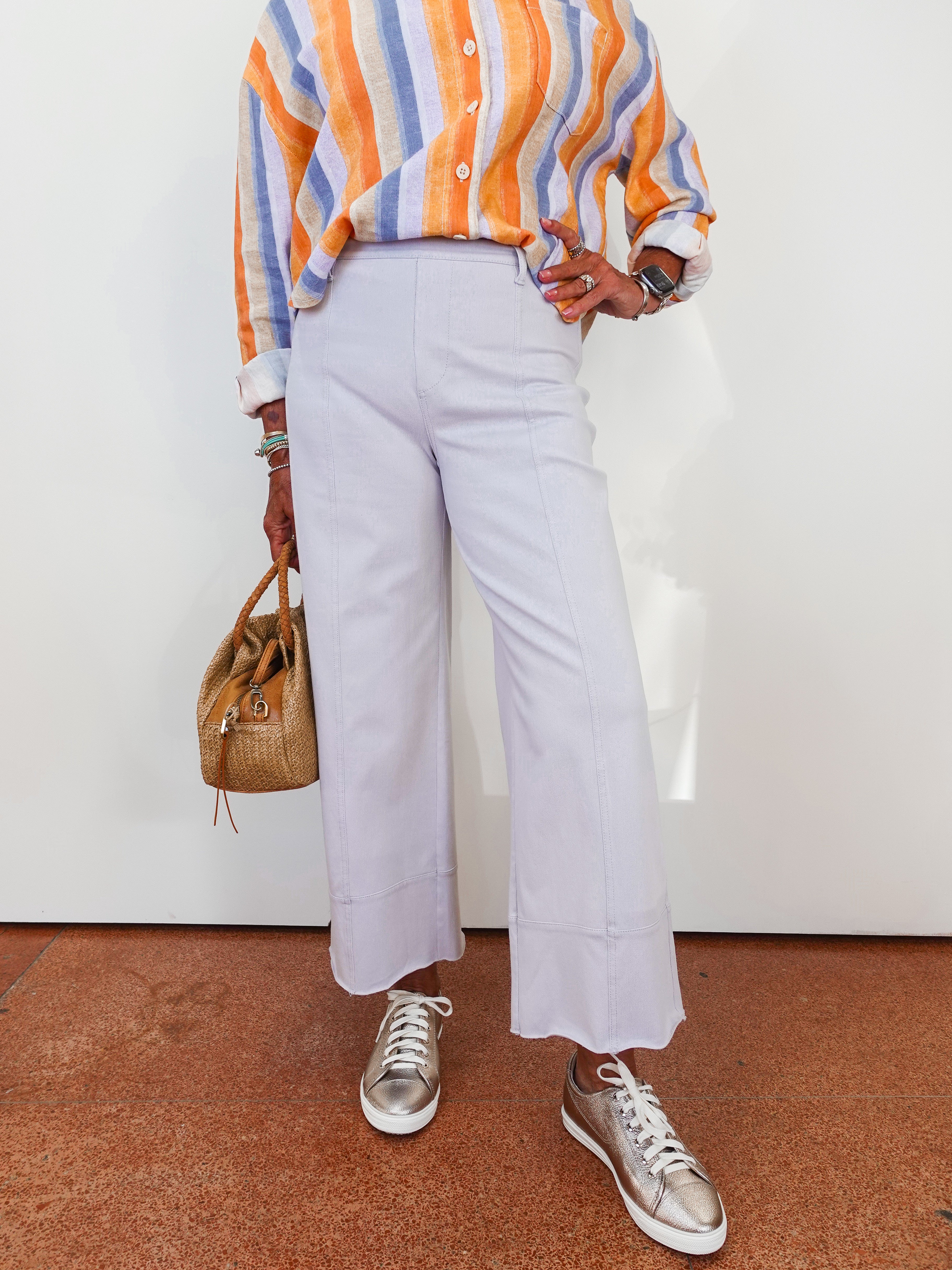 Person wearing a colorful striped shirt, light purple pants, and silver sneakers on a white background.