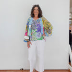 Woman wearing a colorful floral jacket and white pants against a plain background