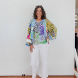 Woman wearing a colorful floral jacket and white pants against a plain background