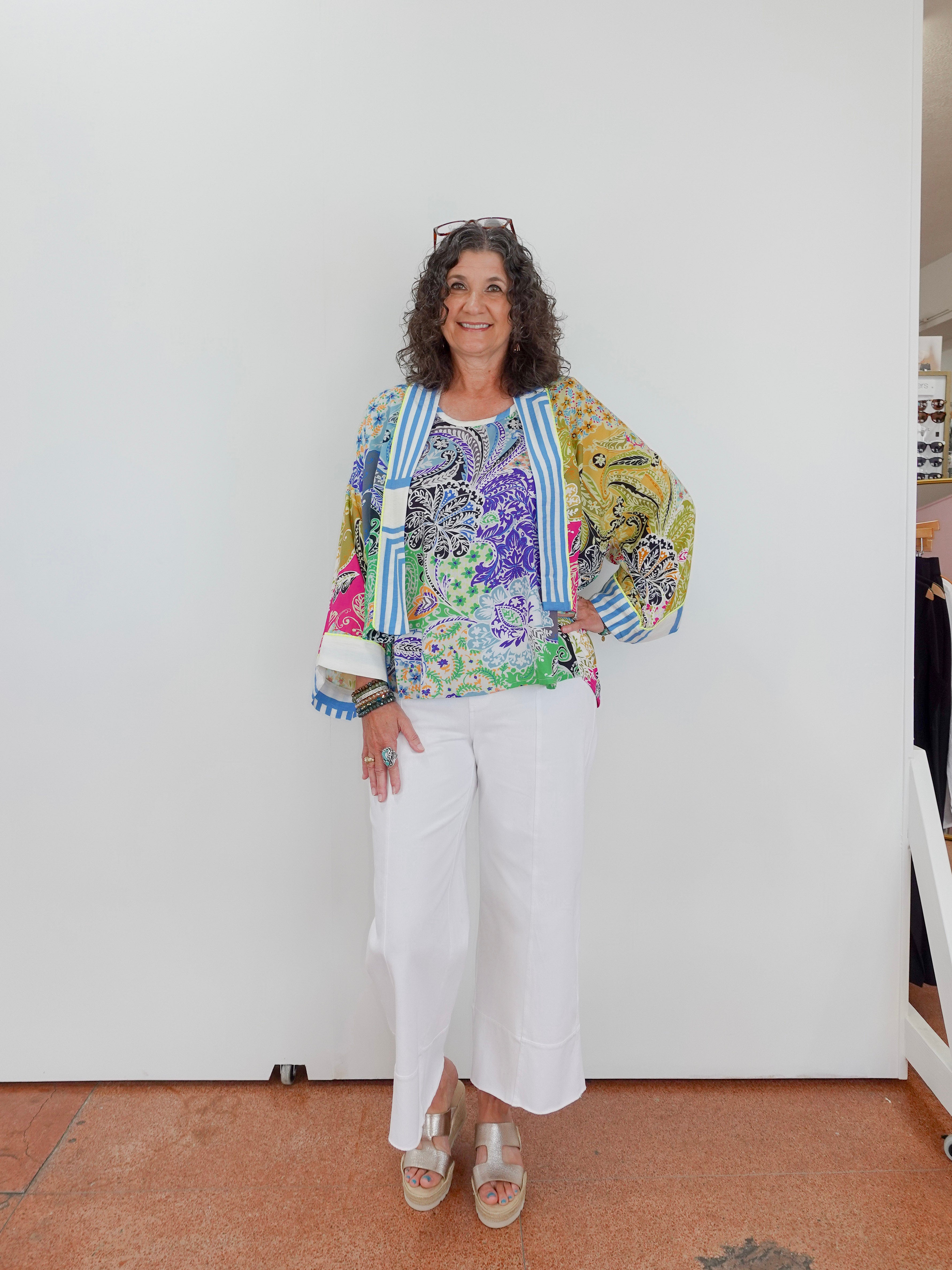 Woman wearing a colorful floral jacket and white pants against a plain background