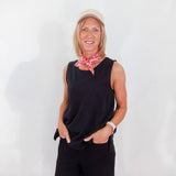 Woman wearing a black sleeveless top and shorts with a red patterned scarf, standing against a white wall.