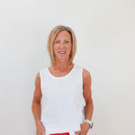 Woman wearing a white sleeveless top and red pants against a plain background