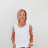 Woman wearing a white sleeveless top and red pants against a plain background