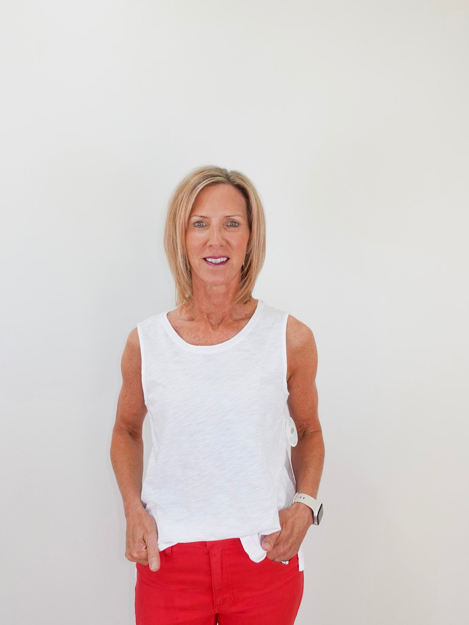 Woman wearing a white sleeveless top and red pants against a plain background
