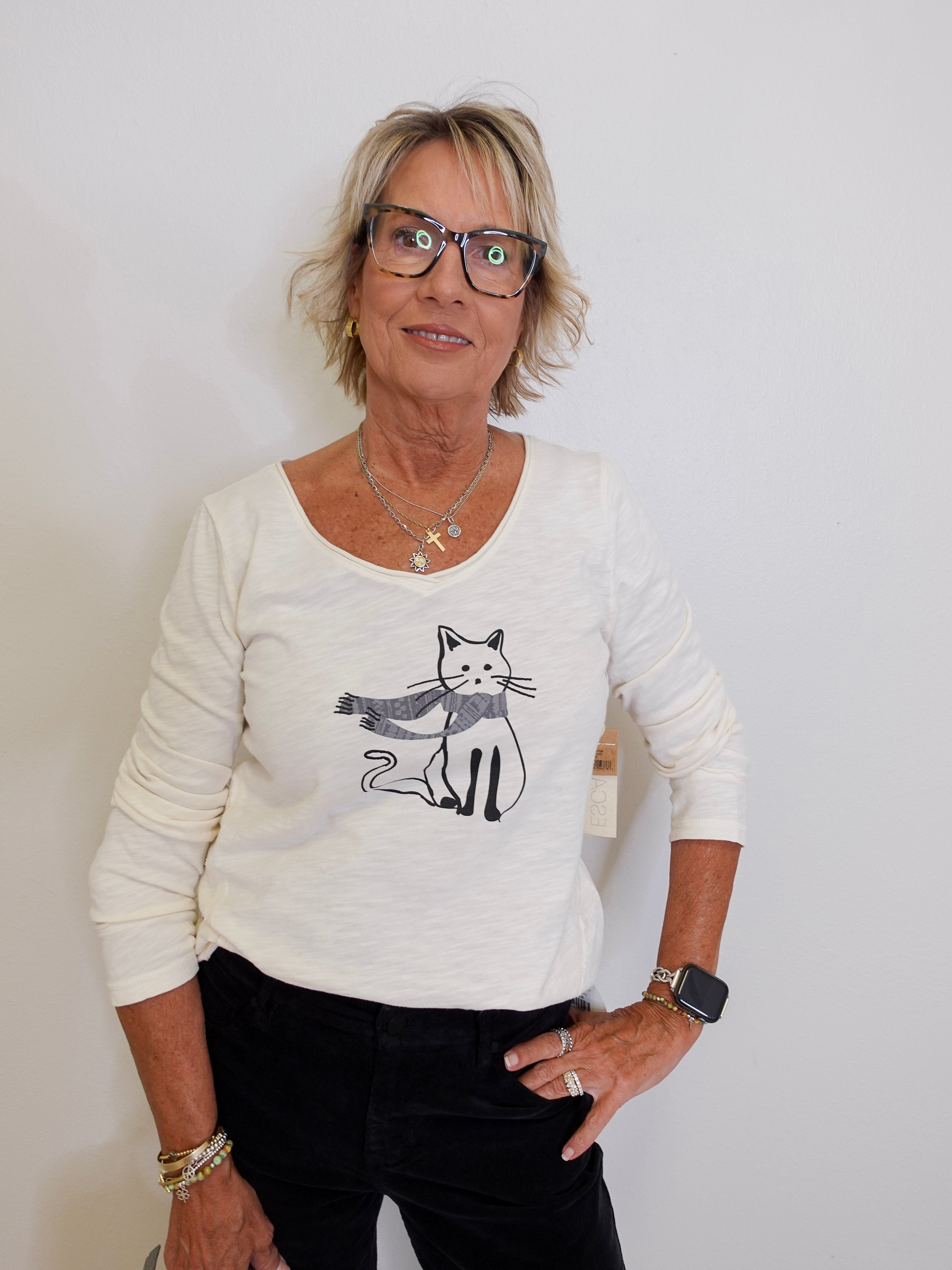 Woman wearing a white sweater with a cat design against a plain background