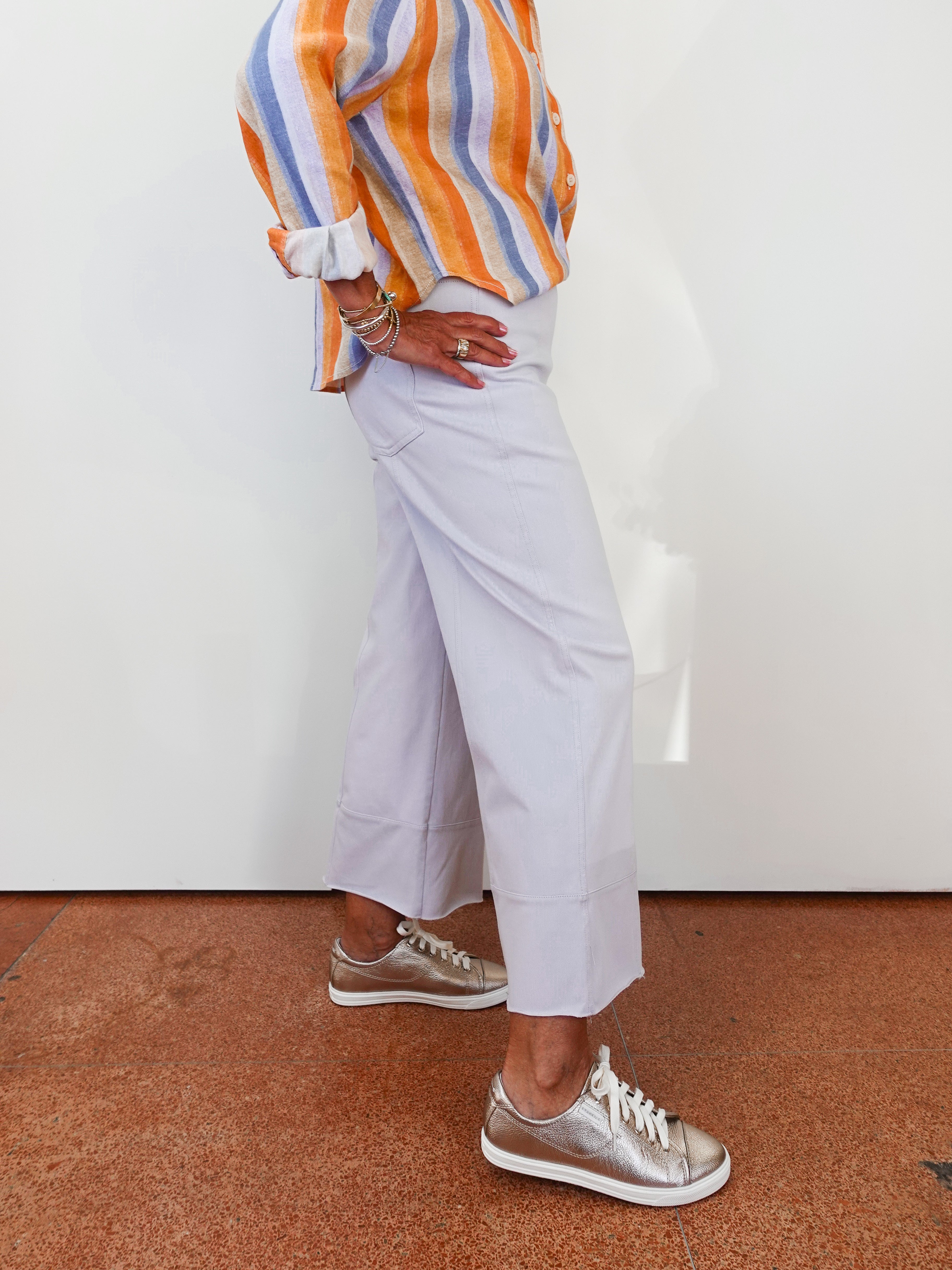 Person wearing a colorful striped shirt, light purple pants, and silver shoes on a white background.