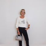 Woman standing against a white wall holding a silver handbag.