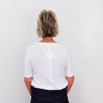 Person wearing a white shirt and dark pants against a plain background