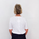 Person wearing a white shirt and dark pants against a plain background