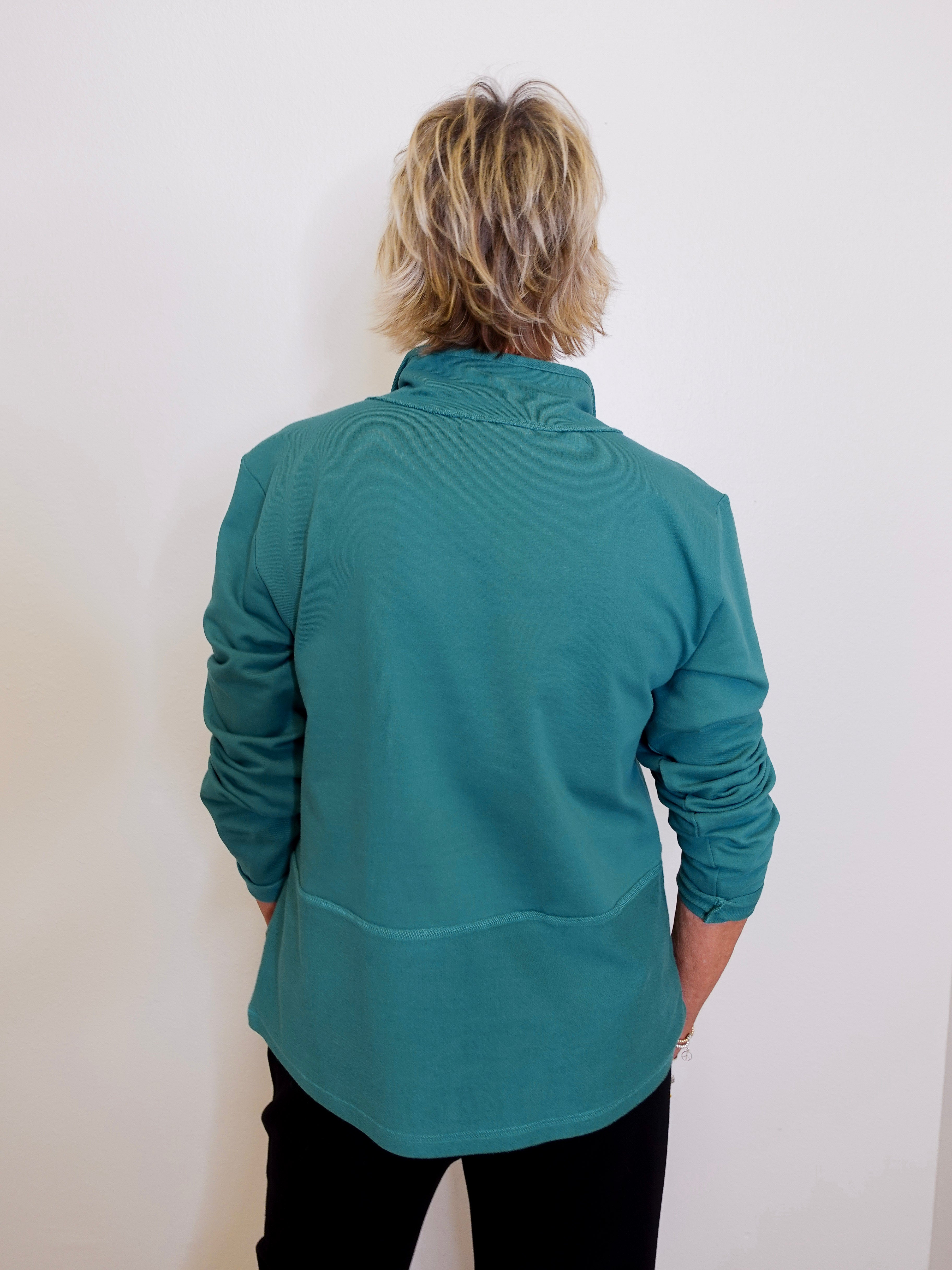 Person wearing a teal long-sleeve shirt against a white background