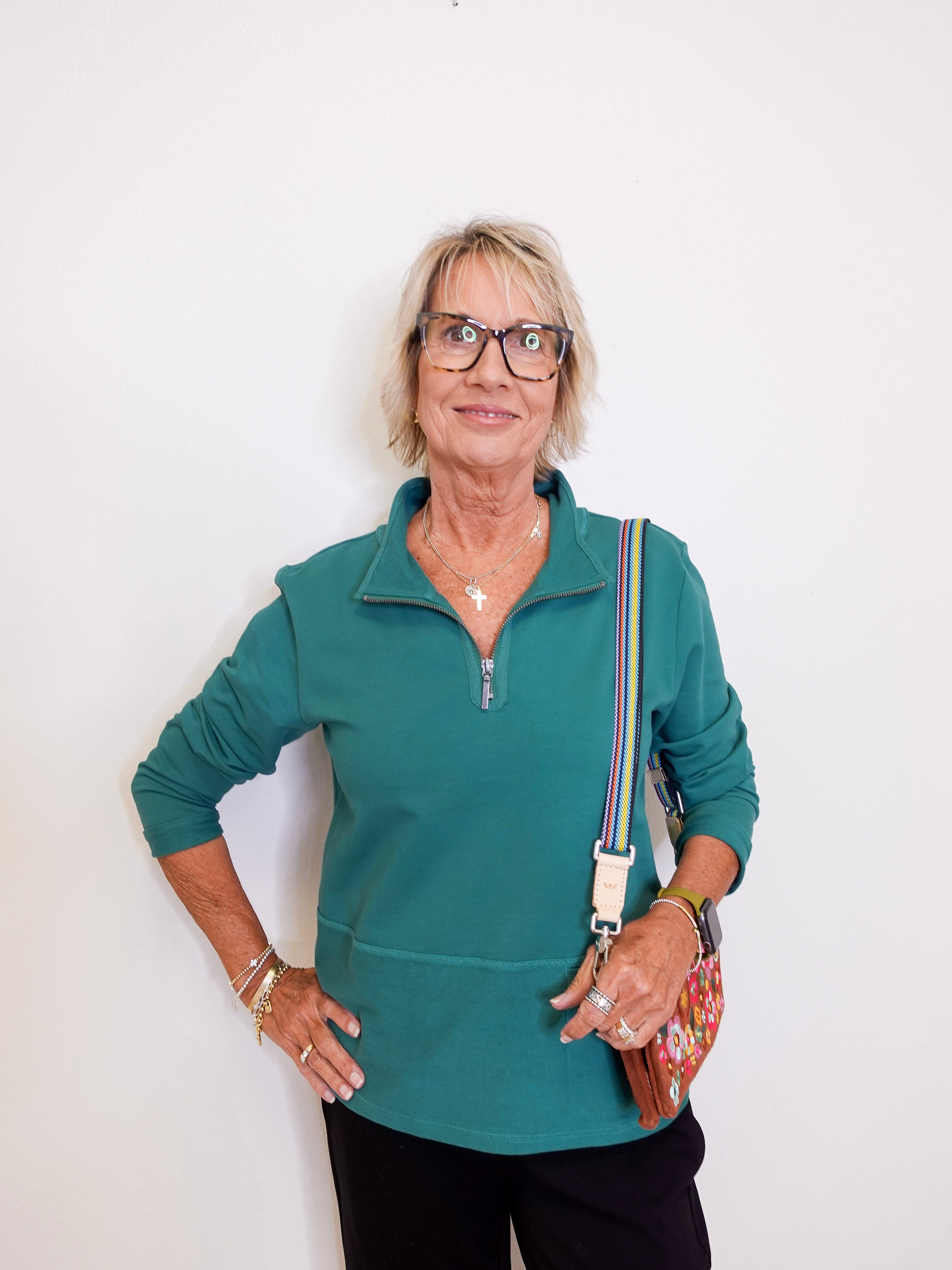 Woman wearing a teal zip-up shirt with a white background