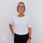 Woman wearing a white shirt and black pants against a plain background