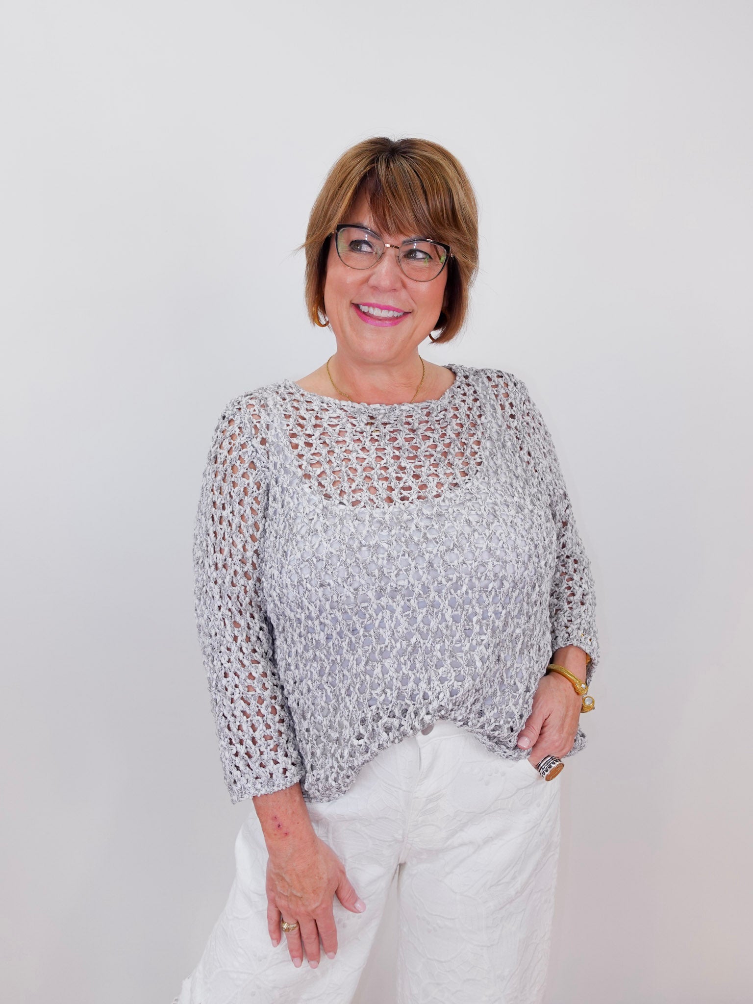 Woman wearing a patterned top and white pants against a plain background