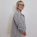 Person wearing a gray jacket and glasses against a white wall
