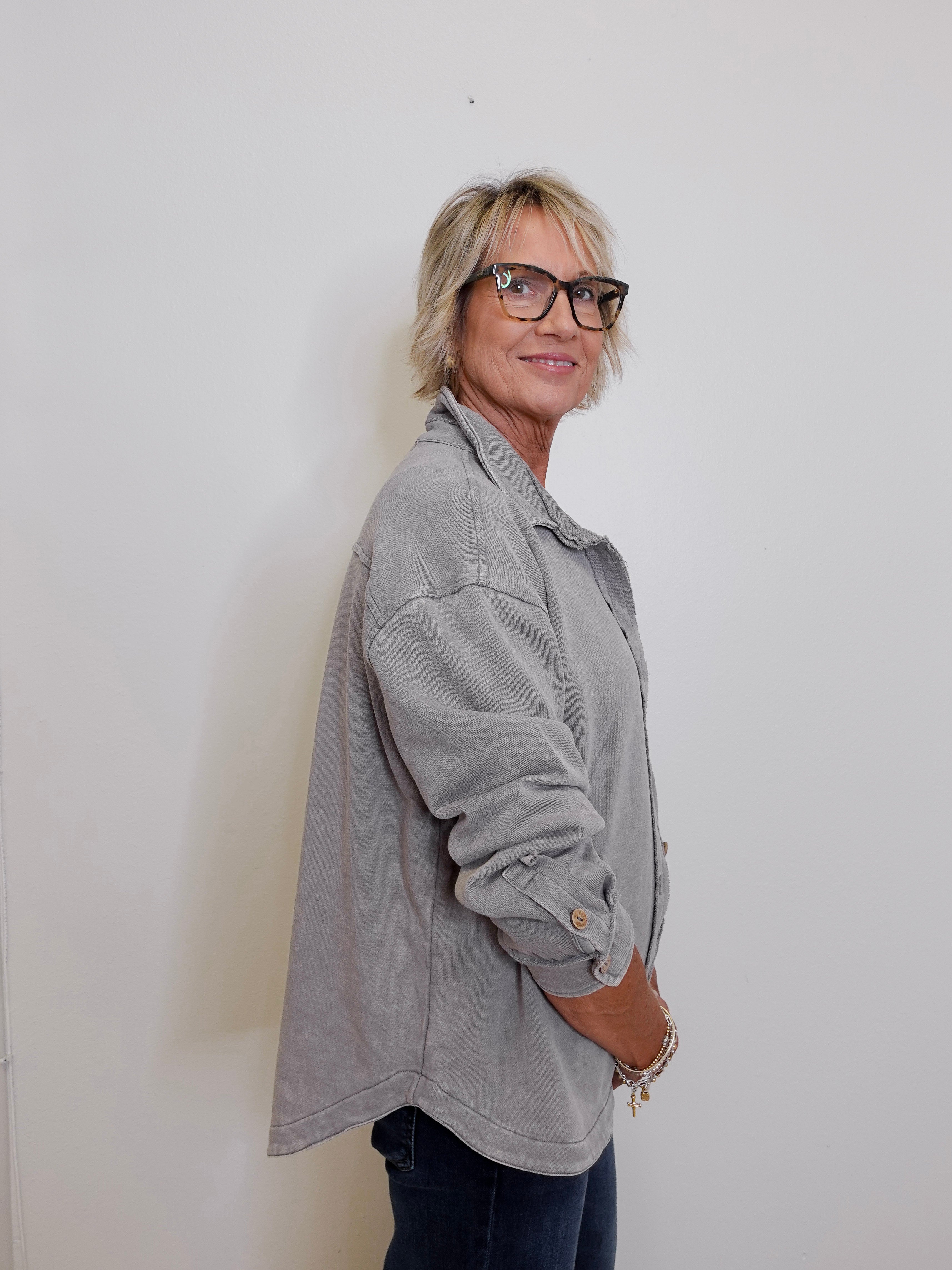 Person wearing a gray jacket and glasses against a white wall