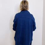 Person wearing a blue jacket standing against a white wall