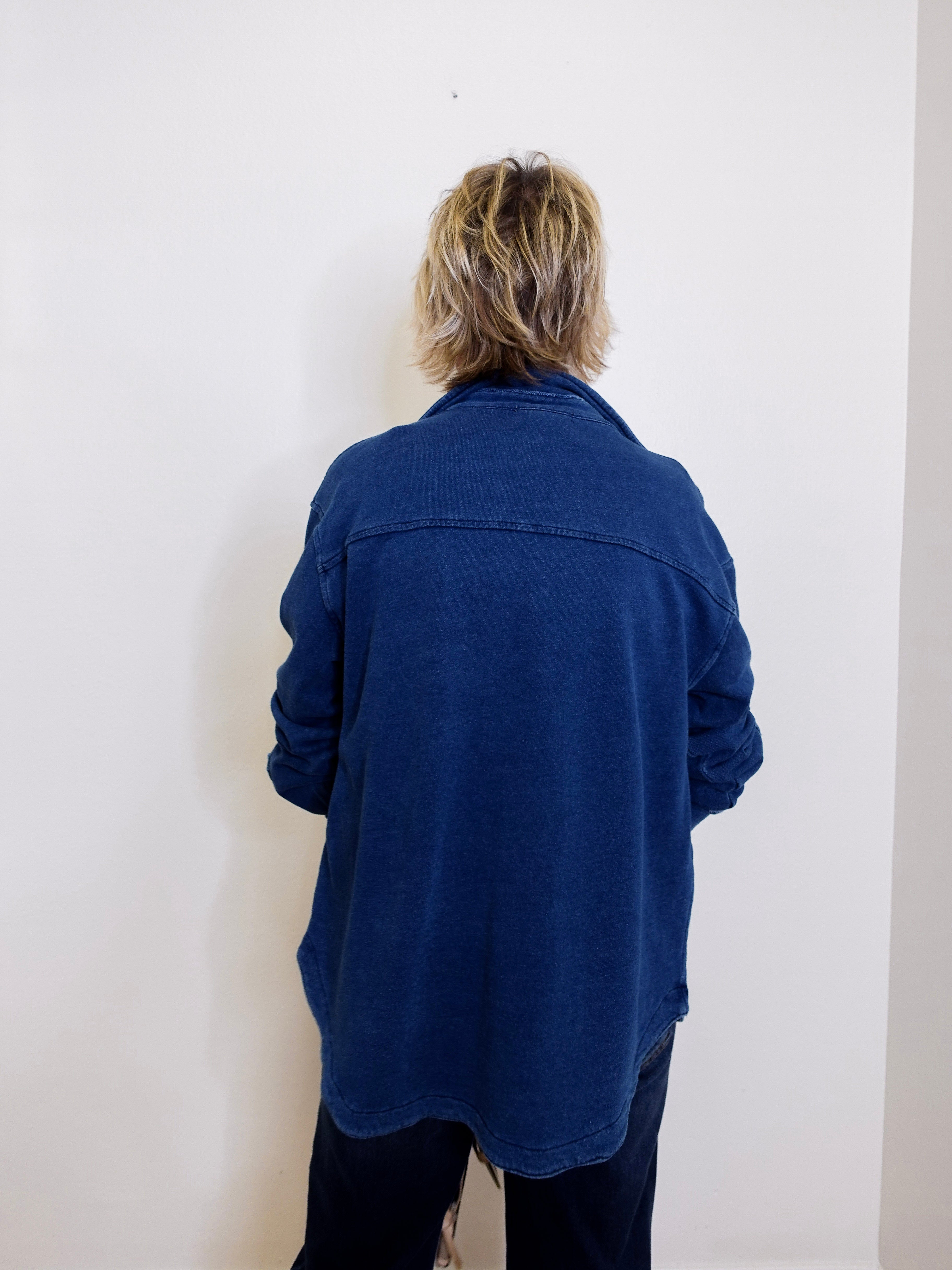 Person wearing a blue jacket standing against a white wall