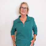 Woman wearing a teal long-sleeve shirt against a white background
