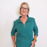 Woman wearing a teal long-sleeve shirt against a white background