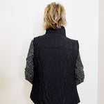 Person wearing a black quilted vest with cable knit pattern on a white background
