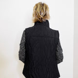 Person wearing a black quilted vest with cable knit pattern on a white background