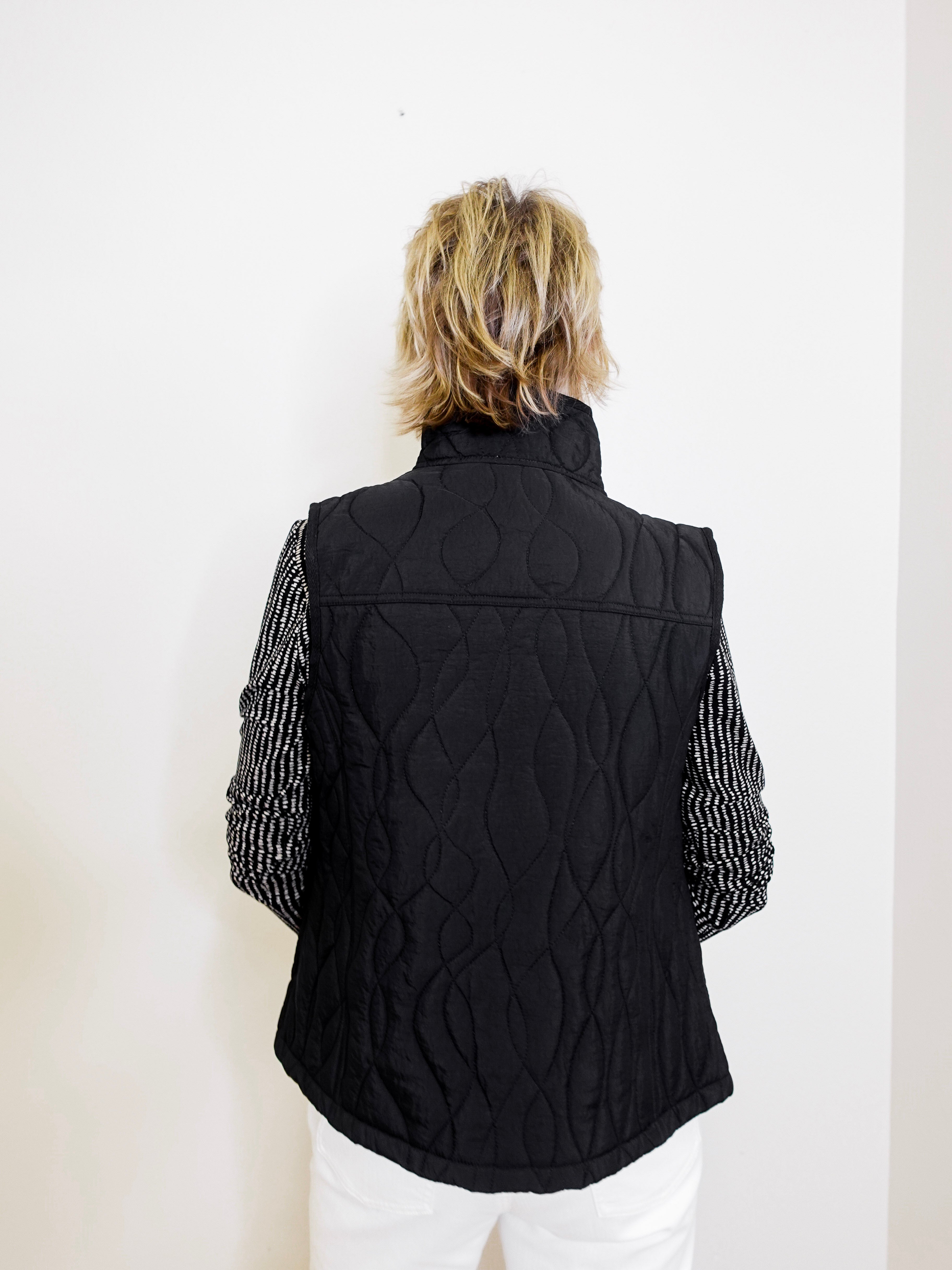 Person wearing a black quilted vest with cable knit pattern on a white background