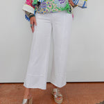 Person wearing a colorful patterned top and white pants against a plain background