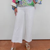 Person wearing a colorful patterned top and white pants against a plain background