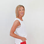 Woman wearing a white sleeveless top and red pants against a plain background