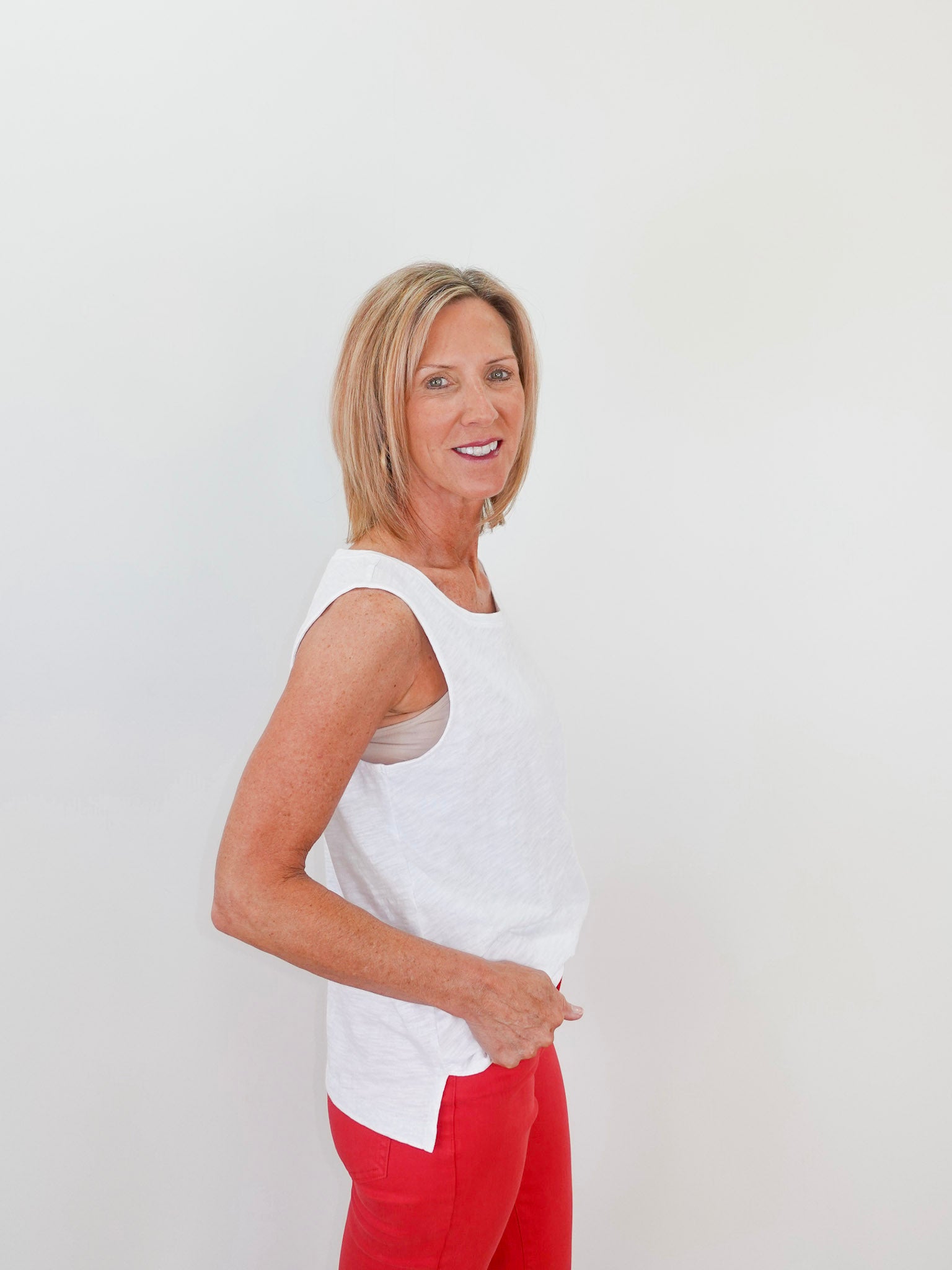 Woman wearing a white sleeveless top and red pants against a plain background