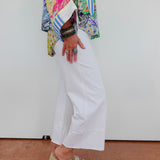 Person wearing a colorful patterned shirt, white pants, and sandals on a plain background